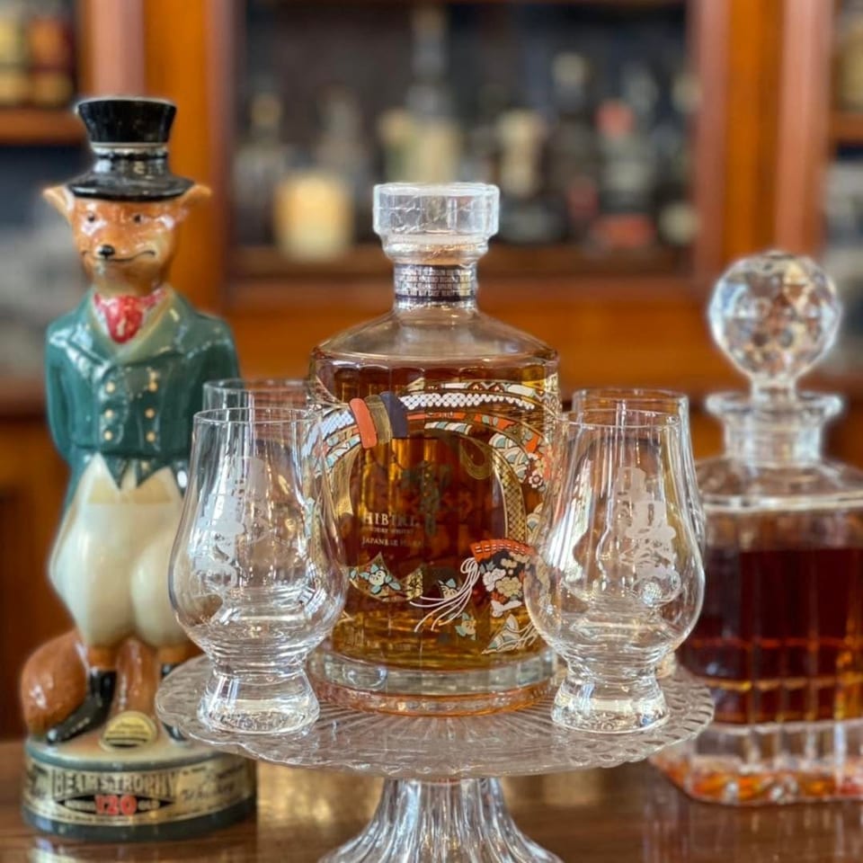 A decorative bottle of Hibiki Japanese Harmony whiskey with two glasses on a stand.