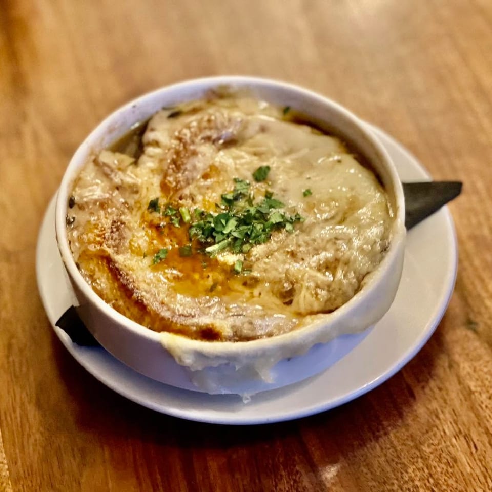 French onion soup in a white bowl with melted cheese and fresh herbs on a wooden table.